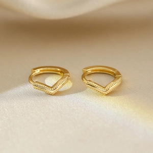 Detailed macro view of V-shaped golden earrings with beaded edges on silk fabric