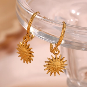 Detailed view of a gold sun face charm earring hanging on a glass rim with a soft background