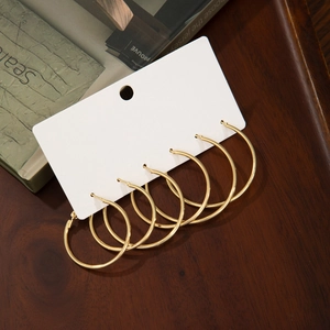 Three pairs of elegant large golden hoop earrings displayed on a white card over wood