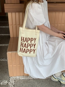 Detail of off-white canvas tote bag featuring brown HAPPY lettering and durable strap
