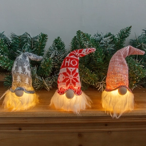 Three glowing Christmas gnomes with knitted hats and LED lights on a festive background