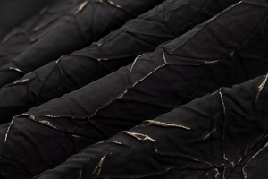 Macro shot of black textured fabric with metallic gold thread and ruched details