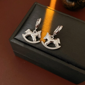 Close-up of silver-tone rocking horse earrings with hammered metal texture on a black box