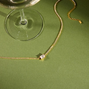 Nahaufnahme einer goldenen Tennis-Kette mit rechteckigem Zirkon auf grünem Hintergrund