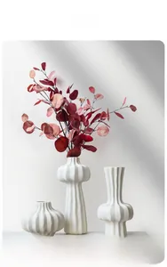 Detail of three white pleated ceramic vases with matte texture and decorative dried leaves