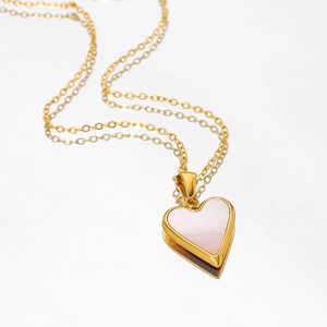 Polished gold stainless steel necklace with a pink heart pendant on white mirror surface