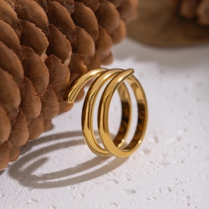 Minimalist golden spiral triple-layer stainless steel ring on natural pine cone background