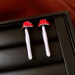 Red mushroom earrings with pearl pendants and silver dots on a black leather display