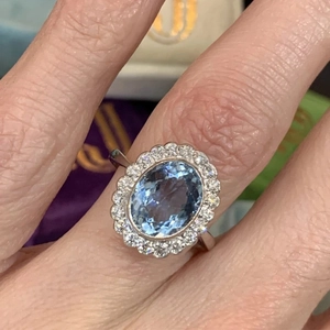 Elegant floral silver ring featuring a large oval blue gemstone with a sparkling diamond halo