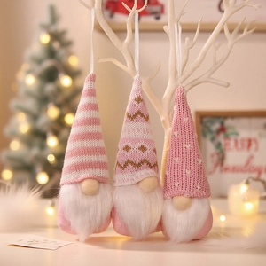 Tre gnomi di Natale rosa lavorati a maglia appesi a rami bianchi con motivi festivi