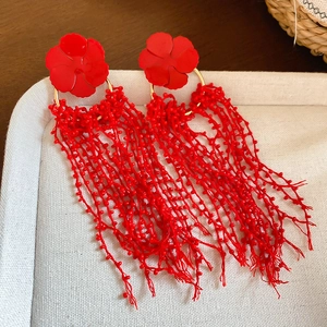 Macro shot of red floral tassel earrings with gold rings and beaded strings on a tray