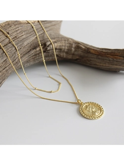 Détail du collier double rang doré avec pendentif pièce Elizabeth II sur support en bois