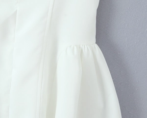 Detailed close-up of white fabric with ruffled pleats and vertical stitching on the dress