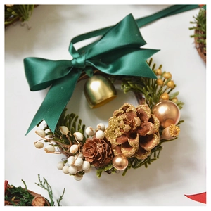 Close-up of Christmas wreath with green bow, golden bell, pine cones and white berries