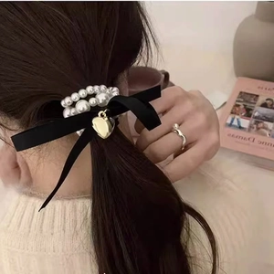 Elegant pearl bow hair scrunchie with a gold heart pendant shown on model