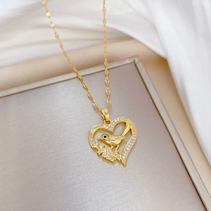 Luxurious gold titanium necklace with sparkling bird and heart pendant on a beige jewelry box