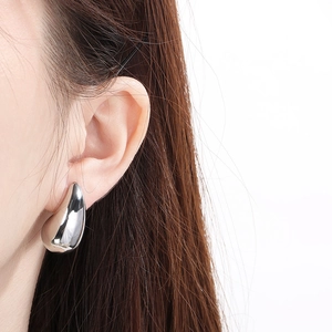 Close-up of polished silver teardrop earring worn by a model in a minimalist style