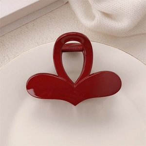 Detail of red heart-shaped butterfly claw clip placed on a decorative white ceramic plate