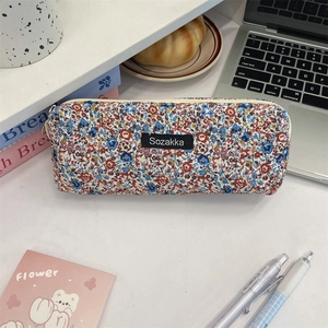 Floral fabric stationery pouch with top zipper and brand label in an office desk setting