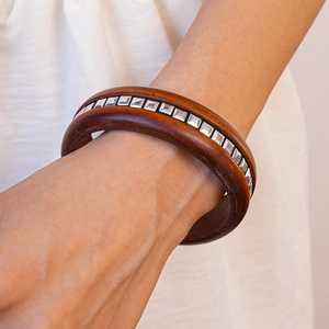 Gros plan d'un bracelet en bois marron foncé rétro avec rivets carrés argentés au poignet