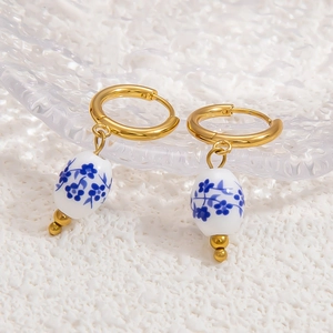Blue floral ceramic teardrop earrings with golden hoops on ripple glass tray