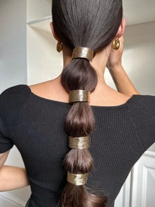 Detail of four golden metallic hair cuffs with brushed texture on long brown hair
