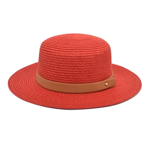 Close-up of red straw sun hat with brown leather strap and golden metallic stud detail