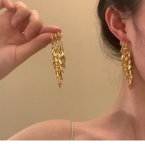 Detail of gold layered leaf tassel earrings showing the elegant long drop style on model