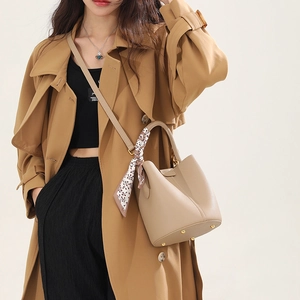 Beige leather bucket bag with top handle and silk scarf shown on a model in trench coat