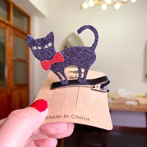 Detail of cute black cat hair clip with red sequin bow on a kraft paper card