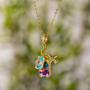 Travel themed gold necklace with blue camera, pink suitcase and small plane charms