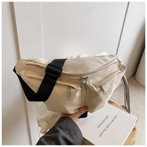 Detail of cream multi-pocket crossbody bag with adjustable black strap and zippers