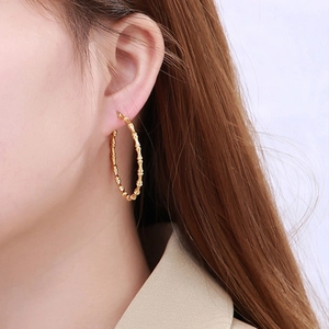 Detail of golden bamboo style hoop earring showing texture and glossy finish on model