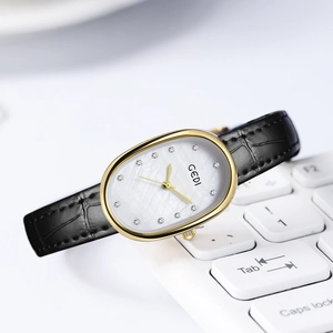 Elegant gold oval watch with pearl dial and black leather strap on white keyboard