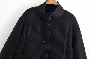 Détail du col montant et de la fermeture à pression sur veste noire en faux daim