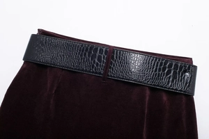 Détail du velours bordeaux avec une large ceinture en cuir noir gaufré crocodile
