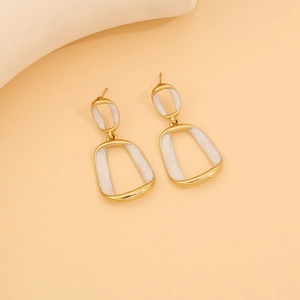 Close-up of golden geometric double-loop earrings with white enamel on apricot background