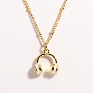 Detail shot of a golden and white enamel headphone pendant on a stainless steel necklace