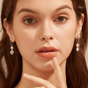 Detail of natural freshwater pearl earring with white clover charm worn on model