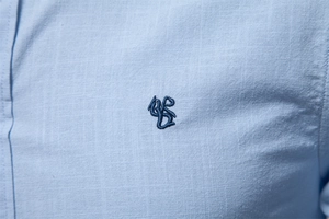 Détail d'une chemise en lin bleu clair avec texture respirante et logo brodé sur le tissu