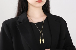 Close-up of golden angel wing pendant on snake chain worn with a formal black blazer