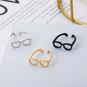 Anillos creativos con forma de gafas en plata, negro y oro sobre mármol blanco