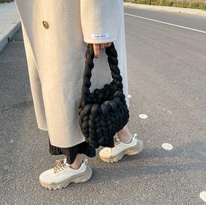 Detail of hand-knitted black chunky yarn handbag with thick knit texture and handle