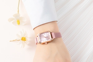 Close-up of a women's rose gold rectangular watch with pink dial and mesh band worn by a model
