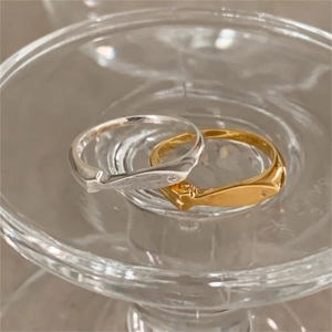 Close-up of minimalist silver and gold fish rings with zircon eyes on glass