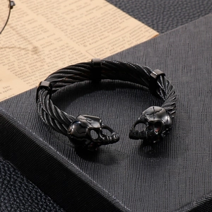 Macro view of men's black braided steel cable bracelet with double skull head detail