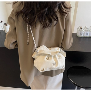 Detail shot of beige ruched cloud bucket bag with metal butterfly and chain strap