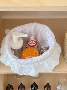 Detailed view of pink plaid fabric basket with white lace trim on a wooden shelf