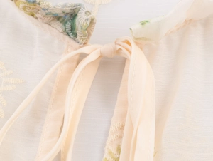 Close-up of beige blouse collar with lace-up ties, green floral ruffles and embroidery