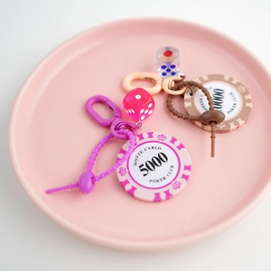 Pink and beige Monte Carlo poker chip keychains with dice on a decorative ceramic tray